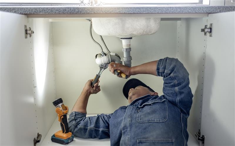 Plumber repairing pipes beneath a bathroom sink in Arcadia